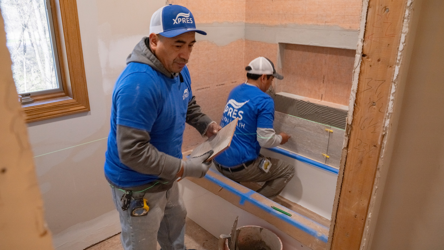 A bath remodel is under way with two construction pros installing a bathtub.